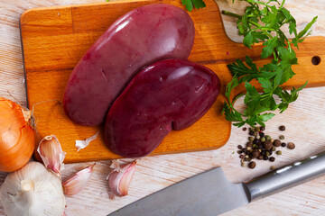 Fresh pork kidneys on wooden background with parsley, garlic and onion