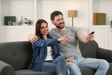 Sticker - Happy couple watching show at home. Man changing TV channels with remote control