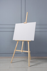 Wall Mural - Wooden easel with blank canvas near grey wall indoors. Space for text