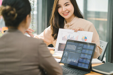 Two businesspeople or an accountant team are analyzing data charts, graphs, and a dashboard on a laptop screen in order to prepare a statistical report and discuss financial data in an office.