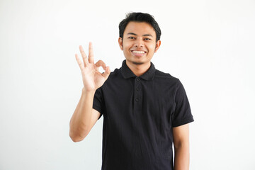 young Asian man smiling friendly while giving OK finger sign wearing black polo t shirt isolated on white background