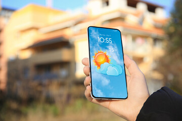 Wall Mural - woman checking weather using app on smartphone outdoors, closeup. data and illustration of sun with 