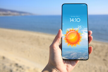 Wall Mural - man checking weather using app on smartphone on beach, closeup. data and illustration of sun on scre