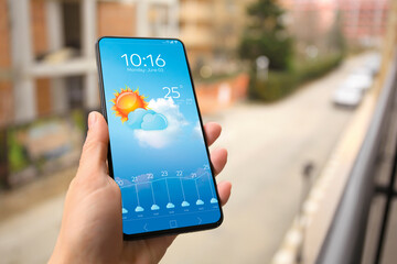 Wall Mural - woman checking weather using app on smartphone outdoors, closeup. data and illustration of sun with 