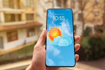 Wall Mural - woman checking weather using app on smartphone outdoors, closeup. data and illustration of sun with 