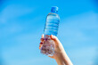 A girl holds a bottle of drinking water in her hand against a blue sky background

