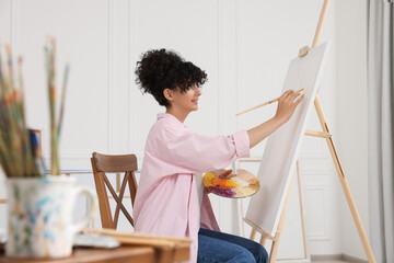 Young woman painting on easel with canvas in studio