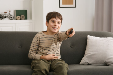 Sticker - Happy boy changing TV channels with remote control on sofa at home