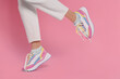 Woman wearing pair of new stylish sneakers on pink background, closeup