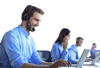 Wall Mural - Smiling male call-center operator with headphones sitting at modern office with collegues on the backgroung, consulting online.