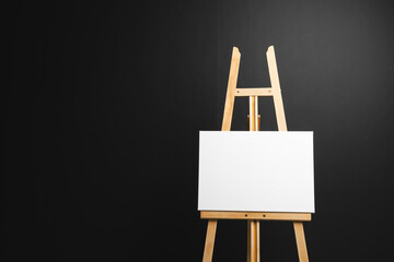 Poster - White canvas on wooden easel and copy space on black background