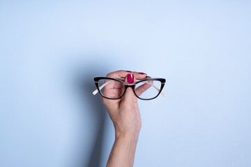 Wall Mural - Eyeglasses in female hand on blue background. Optical store, vision test, stylish glasses concept