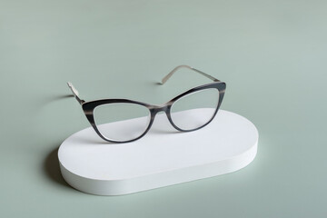 Wall Mural - Podium with eyeglasses on pastel green background. Optical store, vision test, stylish glasses concept.