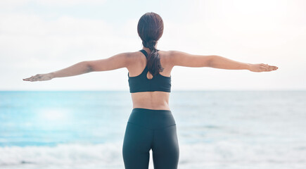 Fitness, freedom and woman back at the beach stretching arms after running or cardio routine in nature. Exercise, rear view and female at the ocean with body stretch for training success or milestone