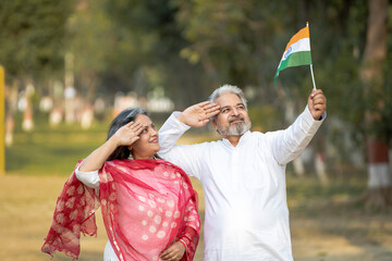 Indian senior couple saluting together of tricolor flag at garden.