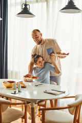 Wall Mural - Positive woman in homewear sitting near boyfriend putting breakfast on table at home in morning