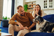 © LIGHTFIELD STUDIOS - Smiling man in casual clothes sitting near border collie and blurred girlfriend on couch at home