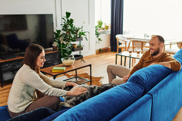 Wall Mural - Smiling woman in casual clothes petting border collie dog near boyfriend on couch in living room