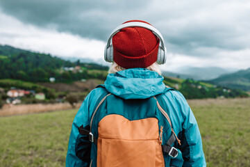 Happy active senior tourist woman listening to music in outdoor leisure trip admiring the landscape feeling inspired by the beauty of nature.