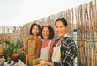 Asian mother with her daughters smiling in front of camera at home terrace - Happy family cooking outdoor on summer day - Main focus on mum face
