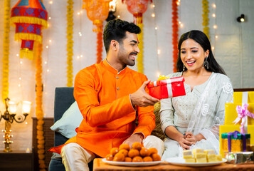 Happy indian brother giving gift or present to sister after tying rakhi at home during raksha bandhan festive celebration - concpet of Sibling Love, Happy Moments and Family Bonding