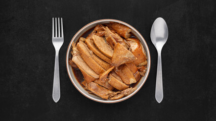 Wall Mural - brown Chinese stewed calf of duck leg in ceramic bowl with fork and spoon on dark tone texture background, top view, flat lay, full HD ratio, Thai food, Ped Pa Lo, Ped Palo, Ped Palow