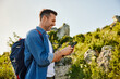 © baranq - Smiling adult man hiking in mountains with backpack navigating with mobile phone