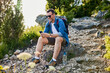 © baranq - Happy adult man sitting on rock using his phone while hiking