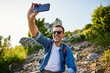 © baranq - Happy adult hiker taking selfie during active weekend in mountains