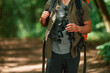 Holds binoculars. Close up view of tourist that is in summer forest