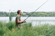 © standret - Standing near the lake. Handsome man in sunglasses is fishing outdoors
