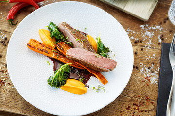 Wall Mural - Duck fillet with sweet potato cream, roasted carrots, kale, beet-port sauce on white plate. Grilled and roasted poultry closeup served on a table for lunch in modern cuisine gourmet restaurant.