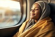 © Stavros - Journey alone with yourself and your thoughts. A young muslim woman rides a train, smiling thoughtfully, looking out the window. Digital detox and offline concept.
