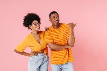 Wall Mural - African man and woman looking away and pointing finger at copy space isolated over pink background