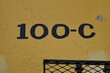 Numéro 100-C. Numéro de rue. Chiffres peints en noir sur mur jaune.