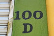 Numéro 100-D. Numéro de rue peint en noir sur mur vert.