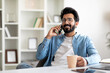 © Prostock-studio - Pleasant Call. Smiling Handsome Indian Man Talking On Cellphone And Drinking Coffee