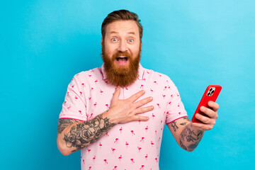 Wall Mural - Photo of impressed speechless man with redhair beard wear pink t-shirt hold smartphone arm on chest isolated on blue color background