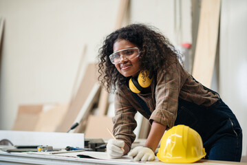 Wall Mural - African American Woman in Safety Hardhat Working in Furniture Factory, Small Business Owner Female Carpenter Working Wood Work in Carpentry Workshop.