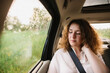 © Denys - Cheerful positive curly young woman in casual wear sitting in automobile backseat with fastened seatbelt and looking away.