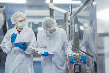 Female factory workers check machine systems at the industrial factory. Women working in clean rooms for beverage and food production