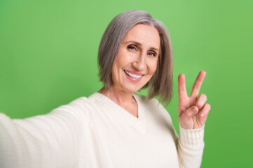 Poster - Closeup selfie blogging retired old lady wear white pullover show v-sign have fun recording her vlog isolated on green color background