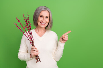 Sticker - Photo of good mood grey hair retired lady wear trendy clothes pointing finger empty space hold cotton flower isolated on green background