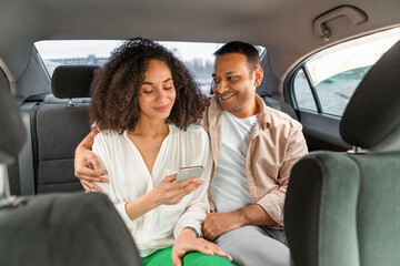 Wall Mural - Smiling Middle Eastern Couple in Taxi Embracing And Using Smartphone