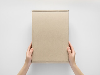 Wall Mural - female hands holding a rectangular cardboard box on a grey background. packaging and delivery concept, top view