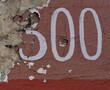Numéro 300. Numéro de rue peint en blanc sur mur abimé. 