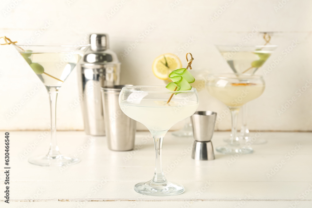 Glass of tasty martini, jigger and shaker on white wooden table