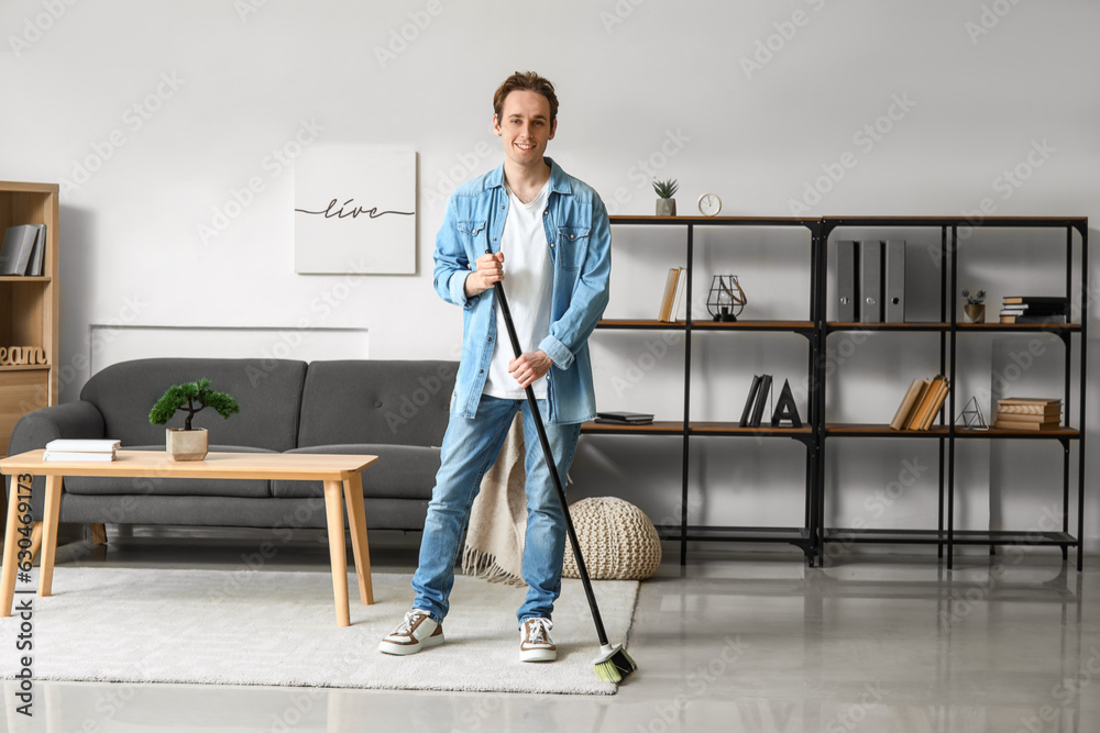 Young man sweeping carpet with broom at home
