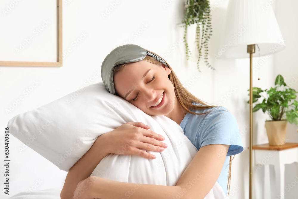 Pretty young woman with soft pillow in bedroom