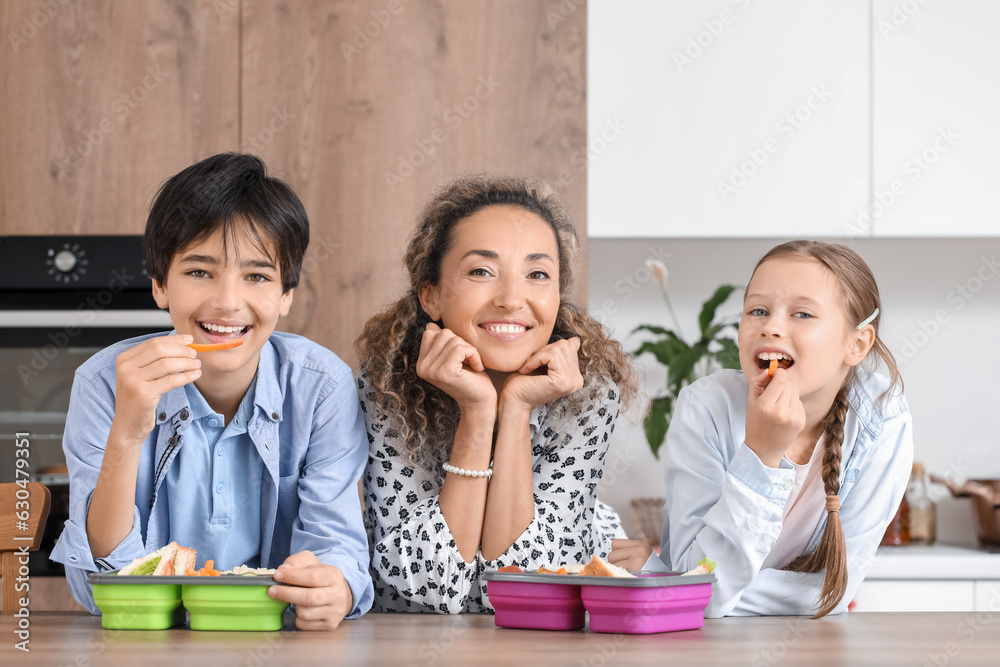 Mother with her little children and school lunchboxes in kitchen